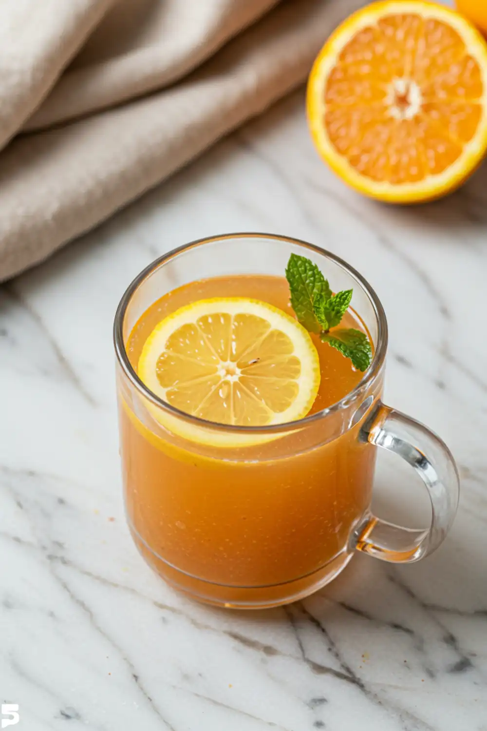 Close-up top-down view of the finished Pink Salt and Turmeric Morning Tonic in a clear mug with subtle wear, showing natural cloudiness and a lemon garnish, looking natural and home-prepared.