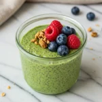 Close-up top-down view of the finished Matcha Chia Seed Pudding in a bowl with subtle wear, garnished with fresh mixed berries and granola, looking natural and home-prepared.