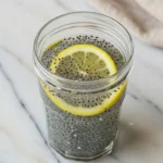 Close-up top-down view of the finished Tadpole Water in a clear glass with subtle wear, garnished with a lemon slice, looking natural and home-prepared.