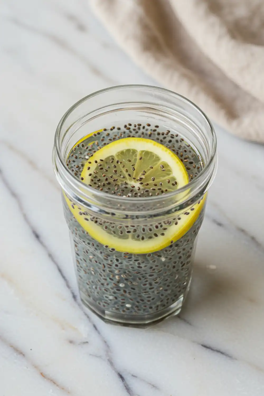 Close-up top-down view of the finished Tadpole Water in a clear glass with subtle wear, garnished with a lemon slice, looking natural and home-prepared.